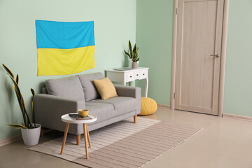 Interior of living room with comfortable sofa and flag of Ukraine hanging on color wall