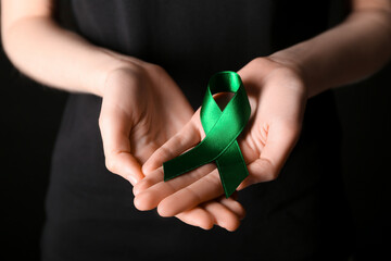 Woman with green ribbon on black background, closeup. Liver cancer concept