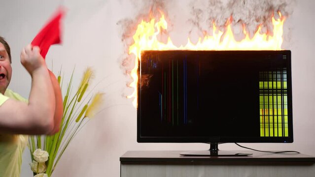 Man extinguishes fire of burning TV in room.