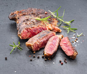Grilled medium rare ribeye steak on gray stone plate.