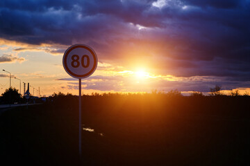 Speed limit sign of 80 km h background bright sunset and clouds.