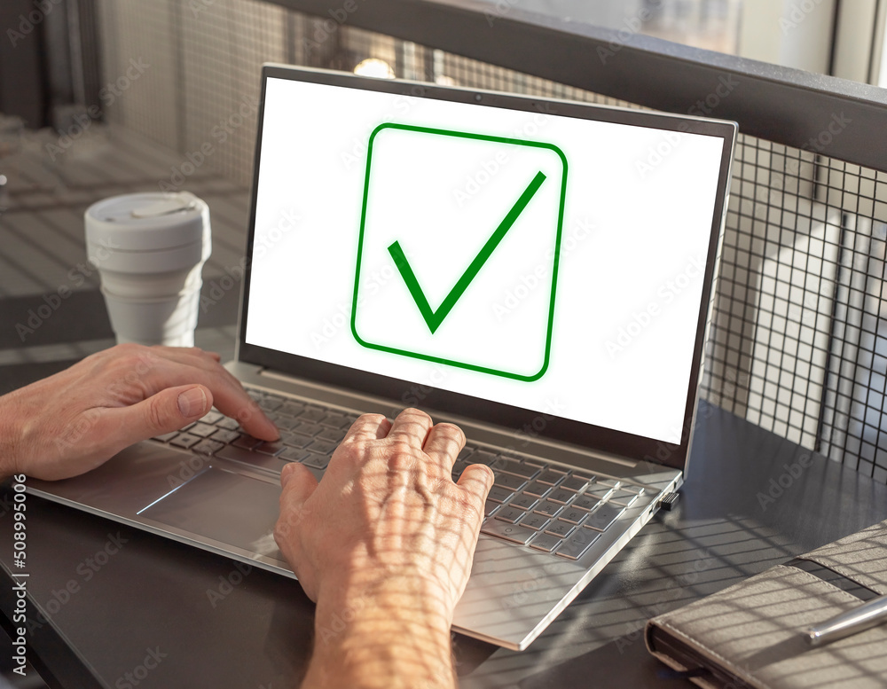 Poster Man hands at laptop keyboard and tick icon at screen. Approval of smth, project verification or data confirmation. Male sitting at table with computer, notebook and takeaway cup. High quality photo