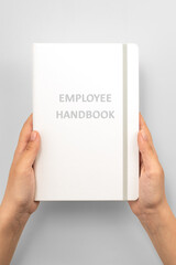 Obraz premium Female hands holding white Employee Handbookon grey background, top view
