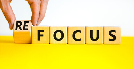 Focus or refocus symbol. Businessman turns wooden cubes and changes the concept word focus to refocus. Beautiful yellow table white background. Business focus or refocus concept. Copy space.