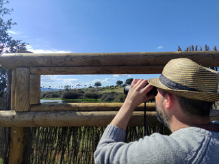 Hombre con prismáticos observando cigueñas en humedal (Malpartida de Cáceres, Extremadura, España)