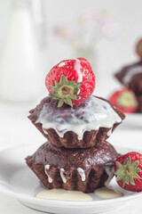 Freshly baked vegan chocolate muffins with red starwberries and white cream on a white plate. Gluten free dessert. Healthy breakfast concept.