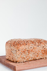 Fresh whole grain bread with sesame seeds on a wooden board. Healthy baked bread on a white background. Copy space.