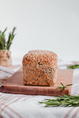 Freshly baked bread with sesame seeds and rosemary on a wooden board. Healthy baked bread on a tablecloth. Copy space.