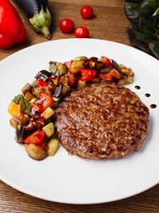 Delicious fried meat patty and vegetable stew. Serving dishes in the restaurant. A hearty lunch, dinner. Photos for the menu. Stewed vegetables - eggplant, zucchini, pepper, tomatoes. Copy space.