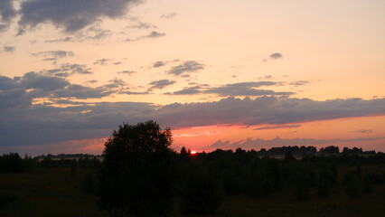 Fototapeta premium Rural landscape with field at sunset and village in the background. Vologda region
