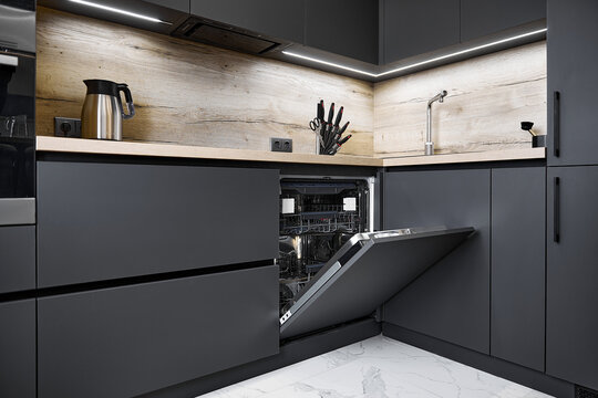 Open built-in dishwasher and dark cabinets in empty kitchen