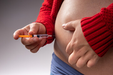 A pregnant woman injects herself a blood thinner with a syringe into her belly to prevent blood...