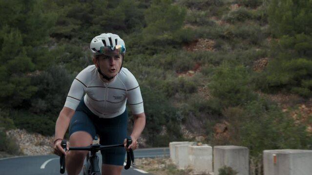 Close up of professional motivated road cyclist screaming, young pretty energetic strong woman ride bike on high mountain top road on daily activity difficult sport intense hard training in warm Spain