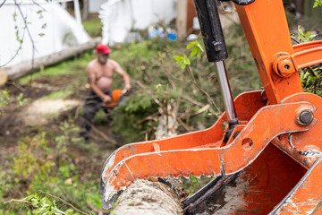 Closeup side profile view, on the hydraulic mechanisms of an excavator boom picking up a tree trunk with blurry workers in background and copy space.