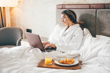 Fototapeta na wymiar Woman eating breakfast and working at laptop in the hotel room.