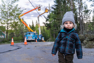 Portrait of a three year old local boy standing on village road as blurry contractors are seen at...
