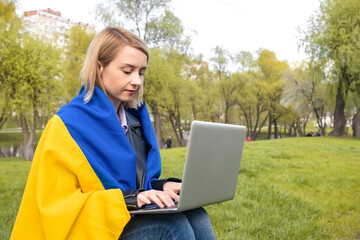 Ukrainian girl with ukraine flag working on laptop in the park. Free lifestyle