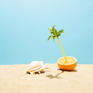 Half orange with drinking straw and mint leaves on the beach sand. Minimal tropical fruits concept. Creative summer vacation idea.