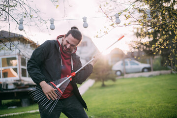 Portrait of a cheerful gardener with a fan rake in his hands, as if with a guitar in the garden at sunset.