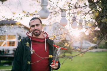 Portrait of a gardener - a young man with a fan rake in his hands in the garden in the evening at...