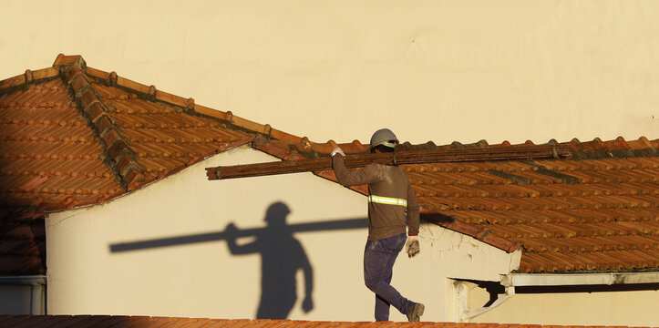 Roofer working on roofing construction. Bricklayer roof repair. House under construction. Workman renovates waterproofing roof of building. Carpenter construction worker carry pile of tiles