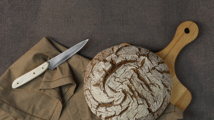 fresh dark bread on a dark background surrounded by a wooden bowl with whole grain flour and a...