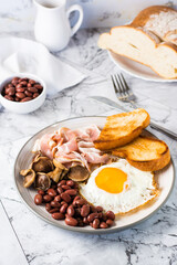English breakfast with fried egg, bacon, beans, mushrooms and toast on a plate. Vertical view