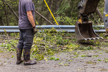 Closeup view of an unrecognizable contractor, standing by the hydraulic arm of a tractor at work clearing a main road of tree debris after storm. © Valmedia