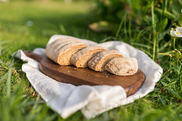 Composition of homemade white flour bread on wood board with white cloth napkin on the green grass . High quality photo