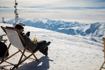 Picture from back of man in armchair, skis, sticks in snowy resort