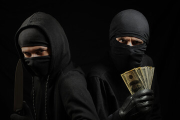 thieves in black masks with a knife and dollars in their hands on a black background. robbers in black balaclava with a knife and dollars in their hands. terrorists in masks. 