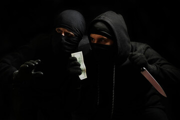thieves in black masks with a knife and dollars in their hands on a black background. robbers in...