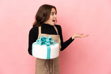 Little Pastry chef holding a big cake isolated on pink background with surprise expression while looking side