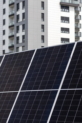 Obraz premium Solar panel photovoltaic cells with apartment building in background, concept of renewable and alternative energy