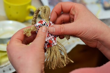 a boy weaves a traditional doll from straw