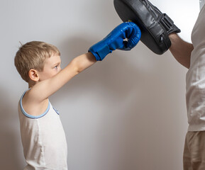 a little boy in boxing gloves trains with a paw held by a man