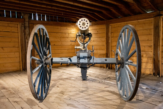 old military gatling gun from the settlement era on wooden cart inside illuminated shed