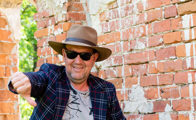 Portrait of middle-aged man in hat and sunglasses on blurred background of old red brick wall