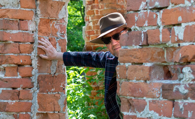 Portrait of middle-aged man in hat and sunglasses on blurred background of old red brick wall