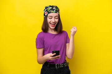 Young Ukrainian woman isolated on yellow background with phone in victory position