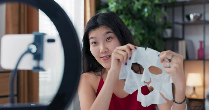 Beauty blogger or vlogger recording product review for brand to share on social media as part of collaboration. Woman holds facial skin care sheet mask in hands tells observers about its benefits.