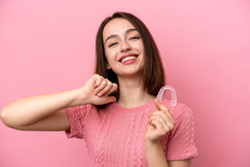 Young Ukrainian woman holding invisible braces isolated on pink background proud and self-satisfied
