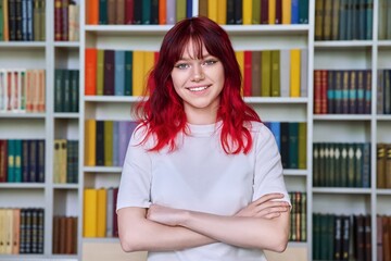 Confident teenage female student with crossed arms looking at camera, portrait in library