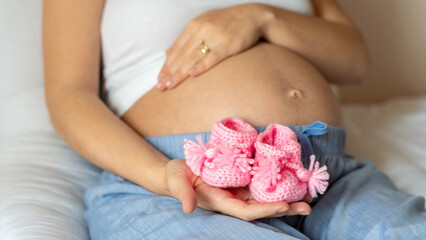 Pregnancy baby shoes. Happy pregnant woman holding pink baby shoes. Small child shoe. Concept of pregnancy, maternity, expectation for baby birth.