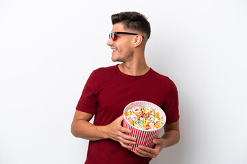 Young caucasian man isolated on white background with 3d glasses and holding a big bucket of popcorns