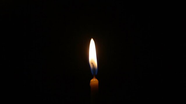 A man lights a thin wax candle in complete darkness. One candle burns at night. The air extinguishes the flame of a burning candle. Looping.