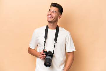 Young photographer caucasian man isolated on beige background looking up while smiling