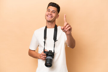 Young photographer caucasian man isolated on beige background showing and lifting a finger