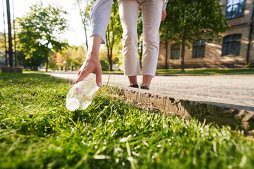 Woman picking up empty bottle as waste in street
