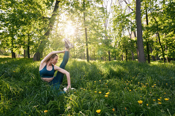 Young sporty woman exercising flexibility in green nature